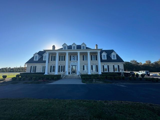 Large white mansion with columns and dormer windows under a clear blue sky