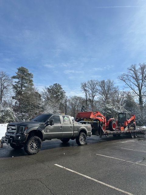 Silver pickup truck towing red snow equipment trailer in a snowy parking lot under a blue sky