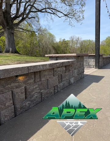 Stone park wall and bench beside a sidewalk, with trees in the background.