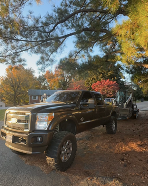 Black lifted pickup truck parked under trees with autumn leaves in a residential yard