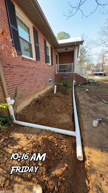 Brick house exterior with exposed white pipes along a muddy side yard at 10:16 AM Friday