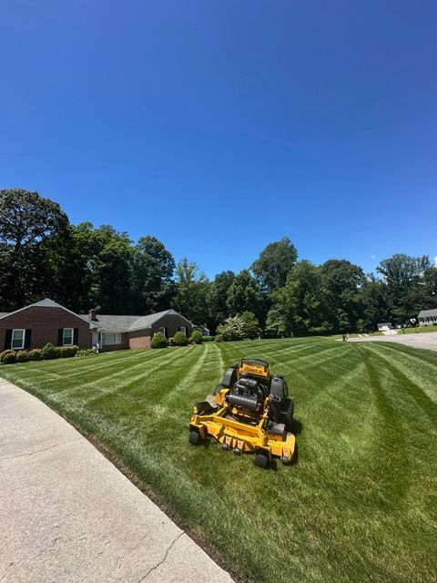 Yellow lawn mower on a freshly cut grassy slope beside a house under a clear blue sky