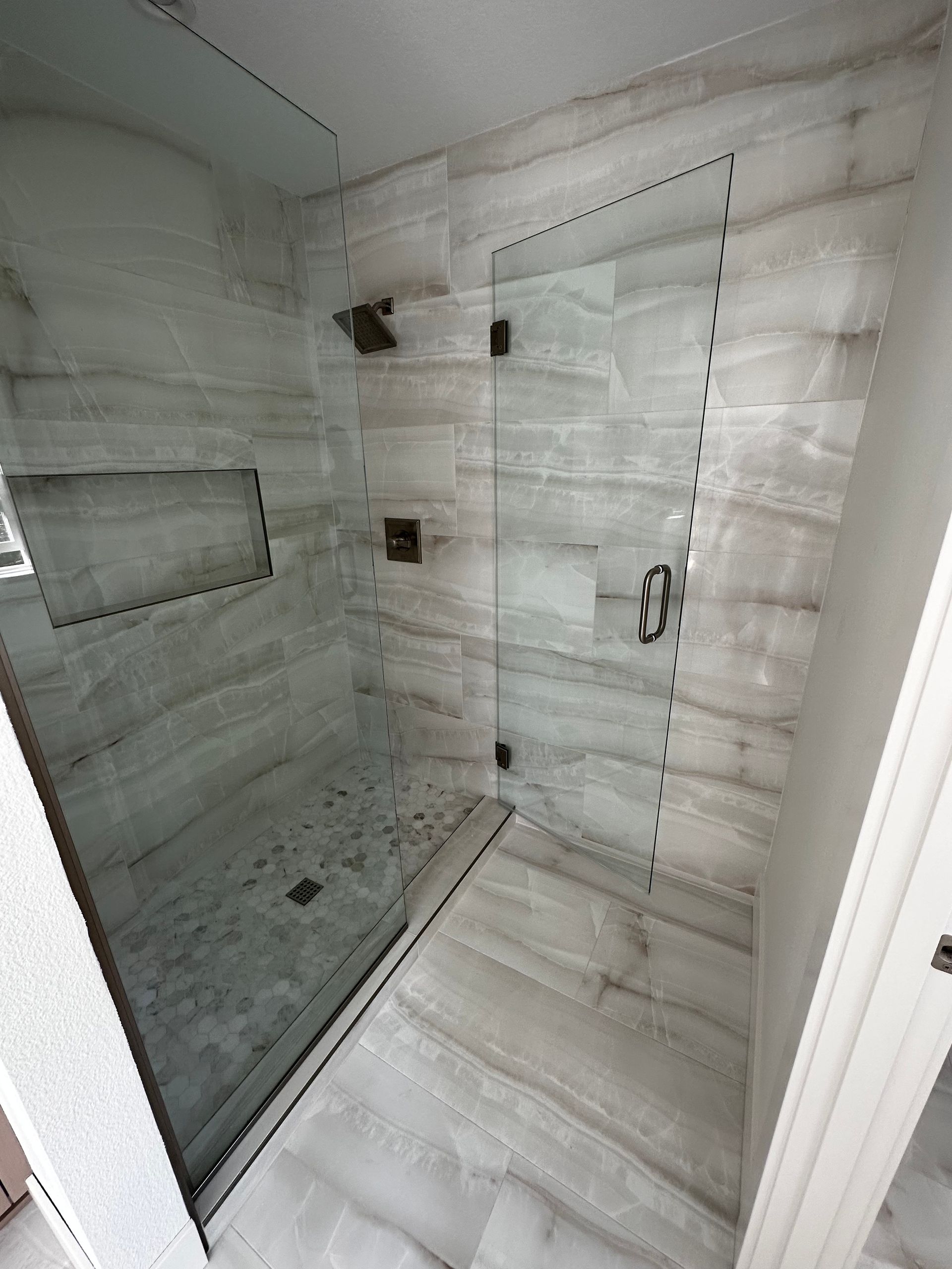 Shower with gray and white tile, glass door, and bronze fixtures.