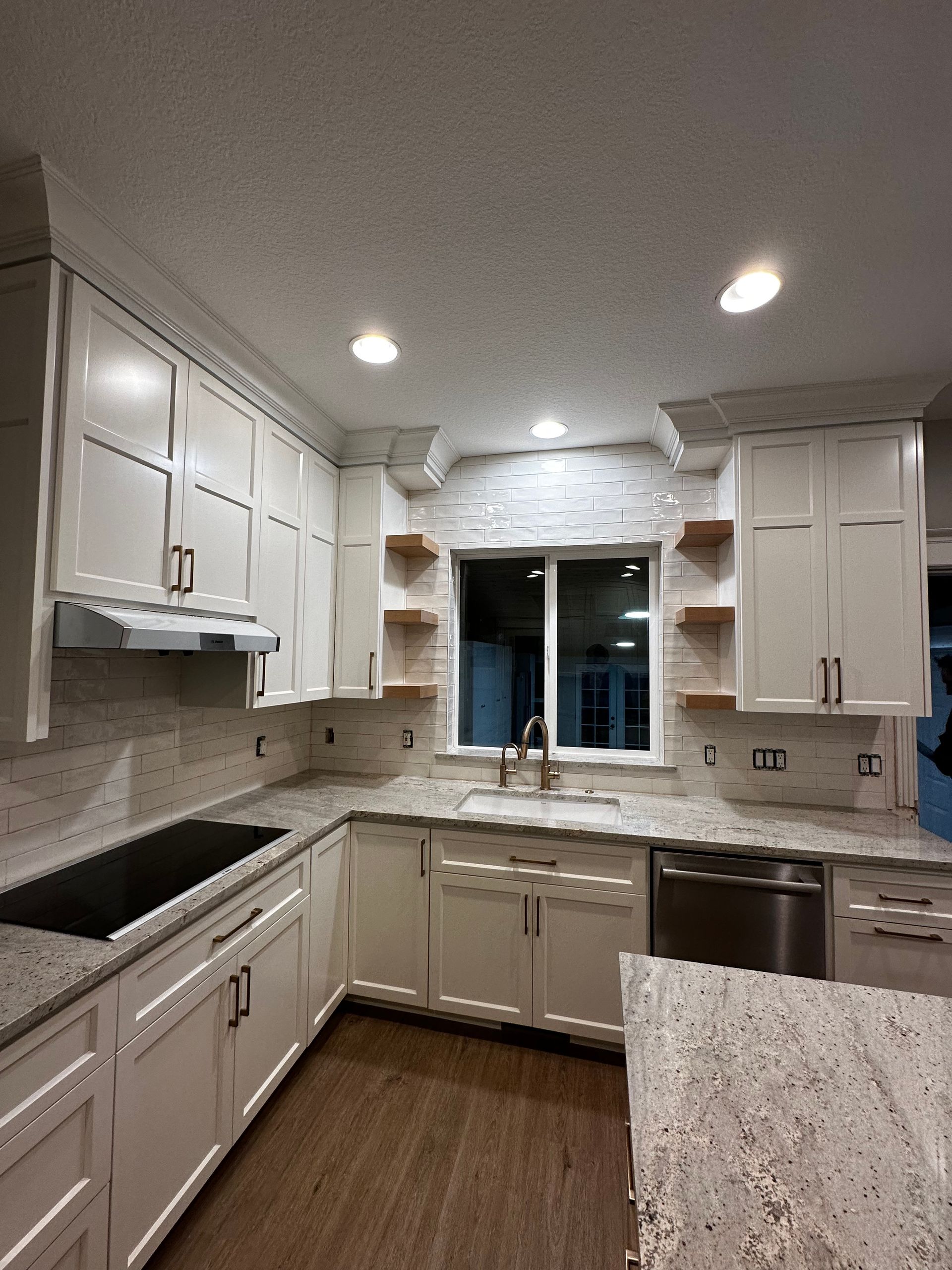 Modern white kitchen with granite countertops, stainless steel appliances, and wood shelves.