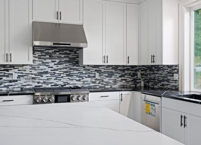 White kitchen with stainless steel appliances, mosaic backsplash, and quartz countertop.