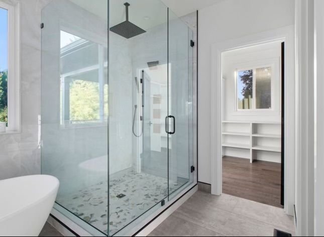 Modern bathroom with glass shower, walk in closet in the background, gray and white tones.