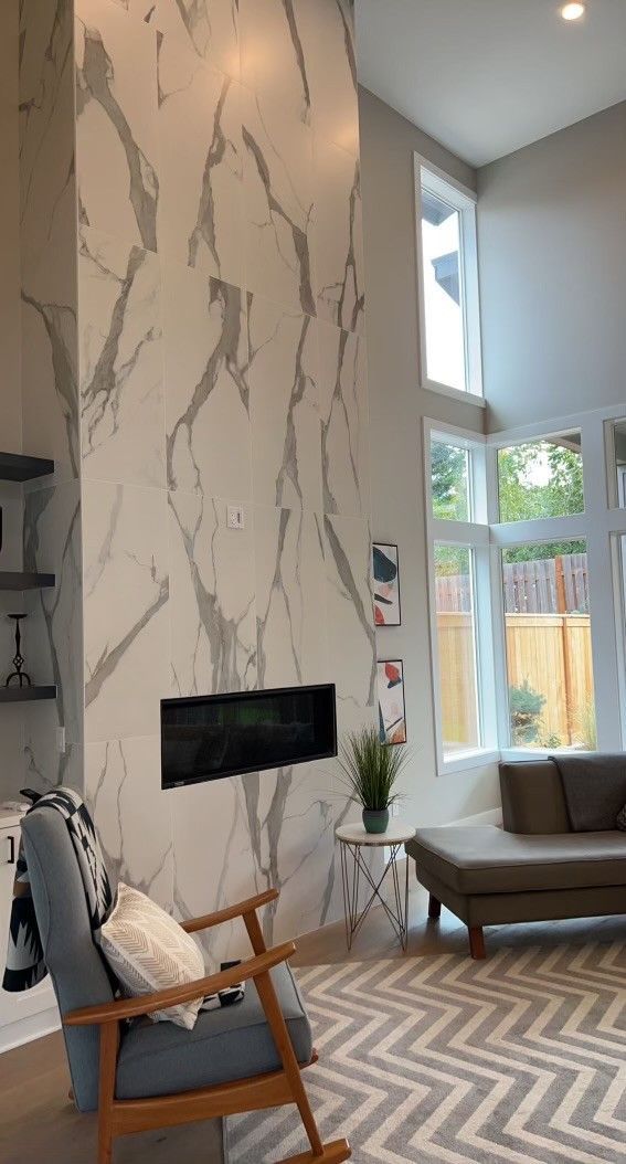 Living room with marble like accent wall, fireplace, large windows, and modern furniture.
