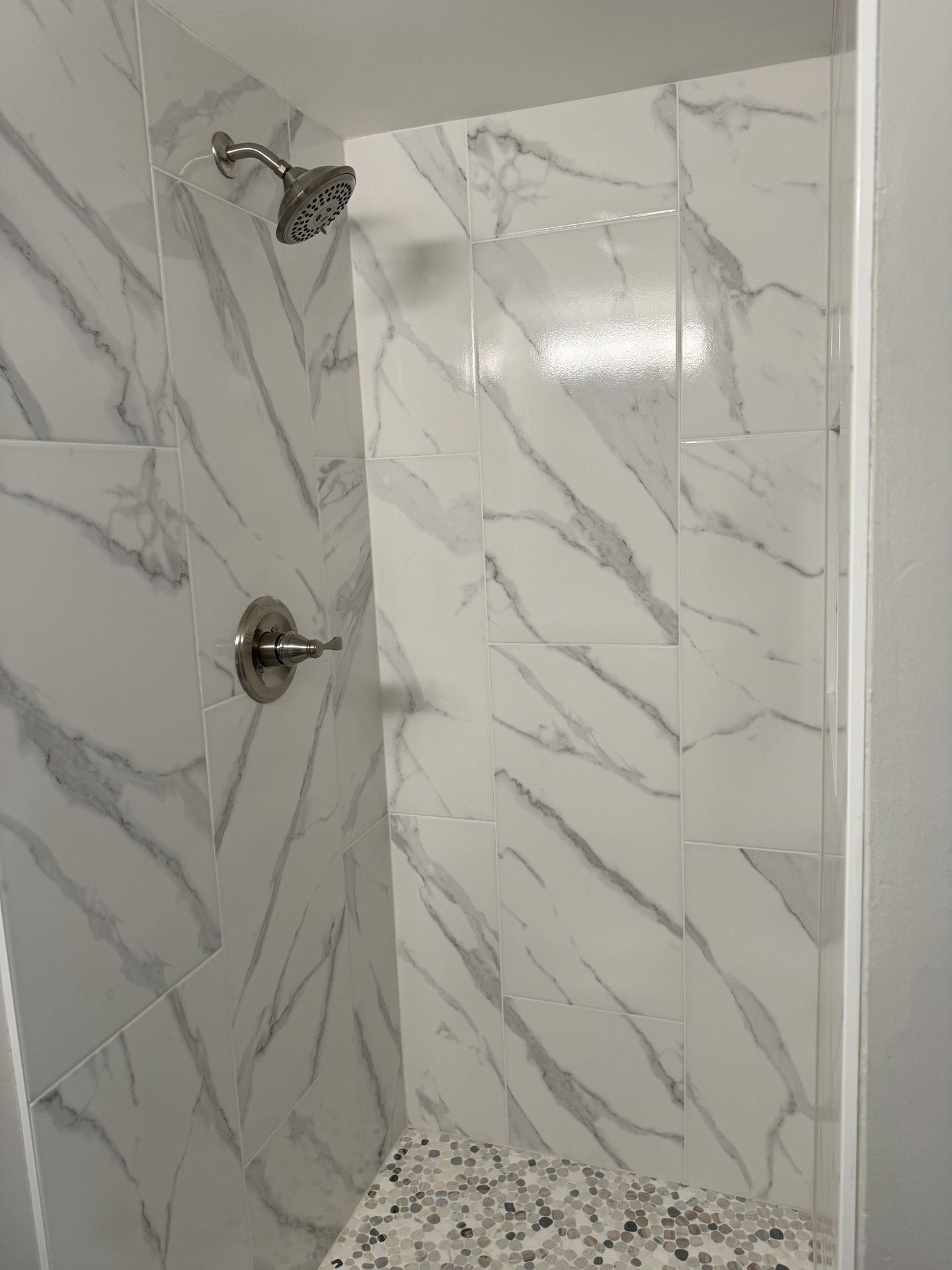 Shower with white marble look tiles, silver fixtures, and a speckled bench.