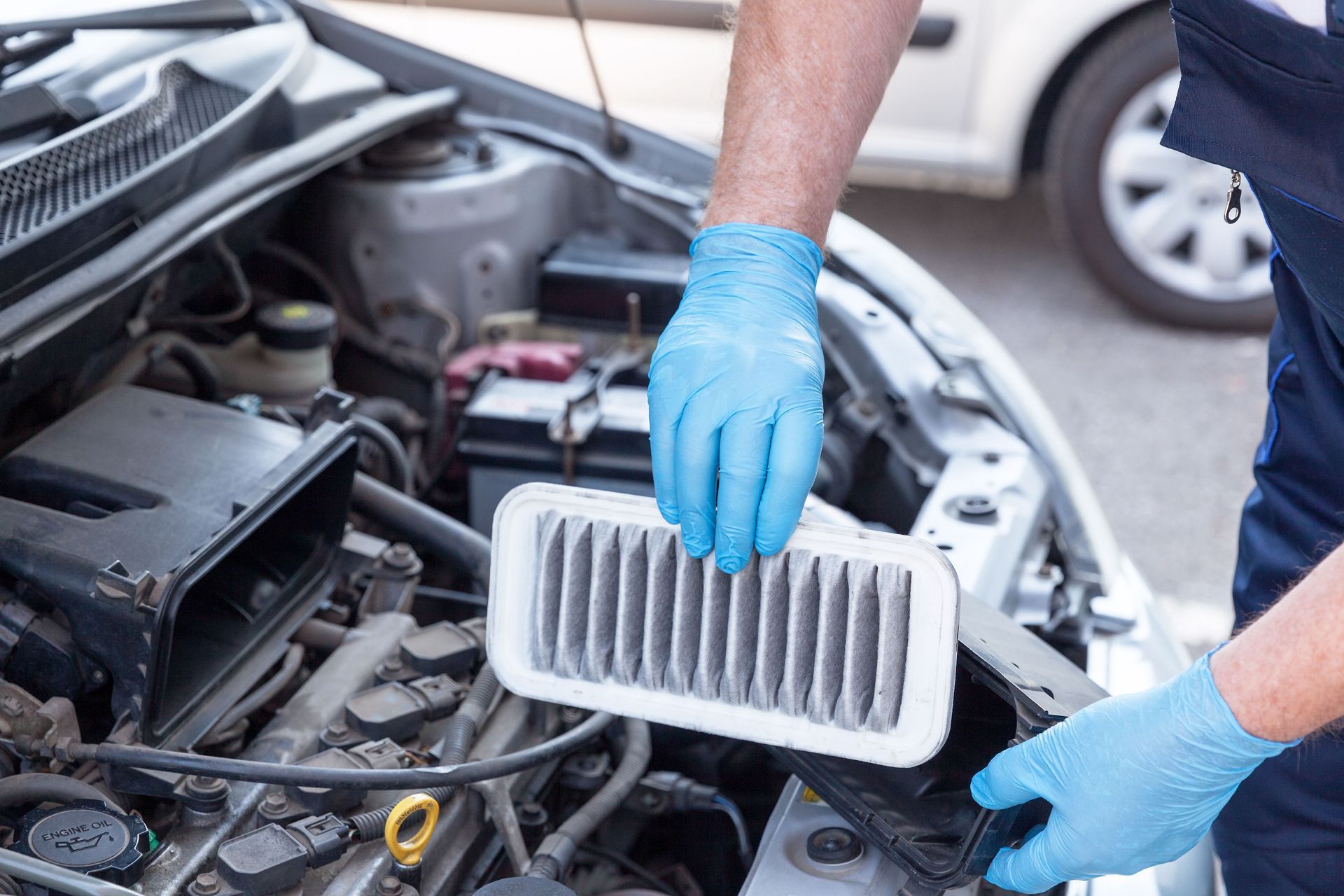 Mechanic in blue gloves replacing a car engine air filter under the hood