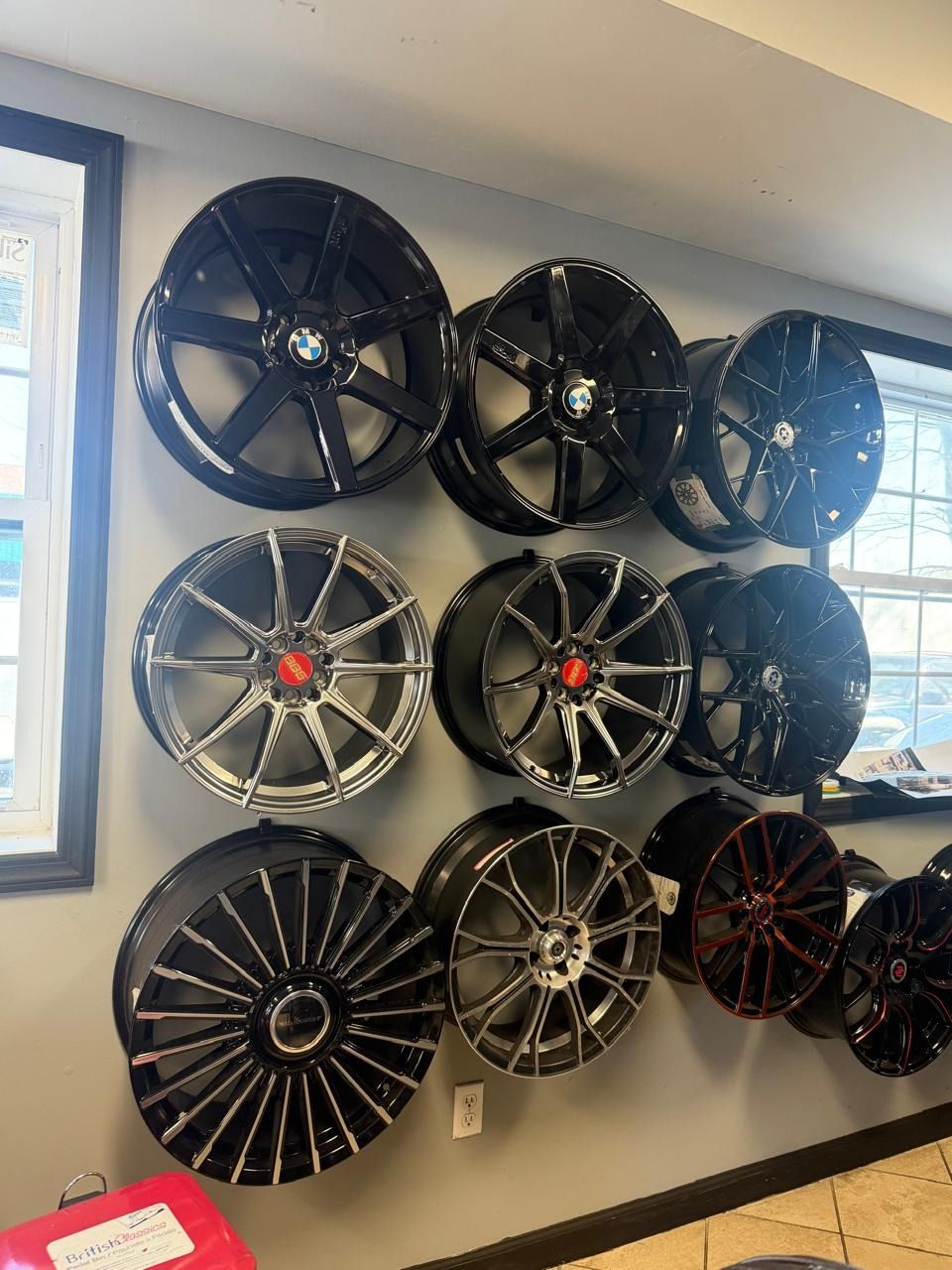 Wall display of assorted car rims in black, silver, and red accents inside a showroom or shop