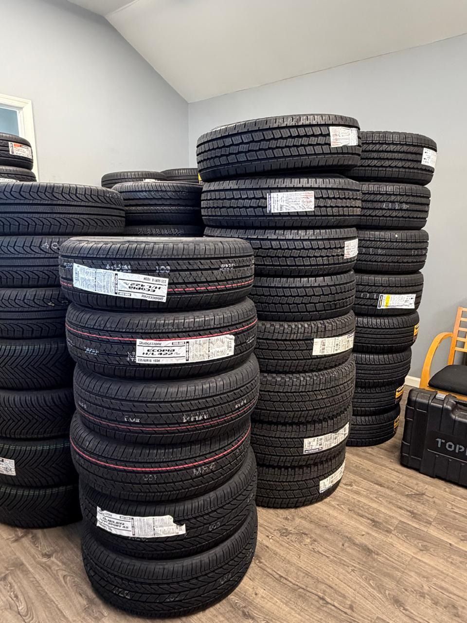 Stacks of black tires piled in a storage room with light walls and wood flooring.