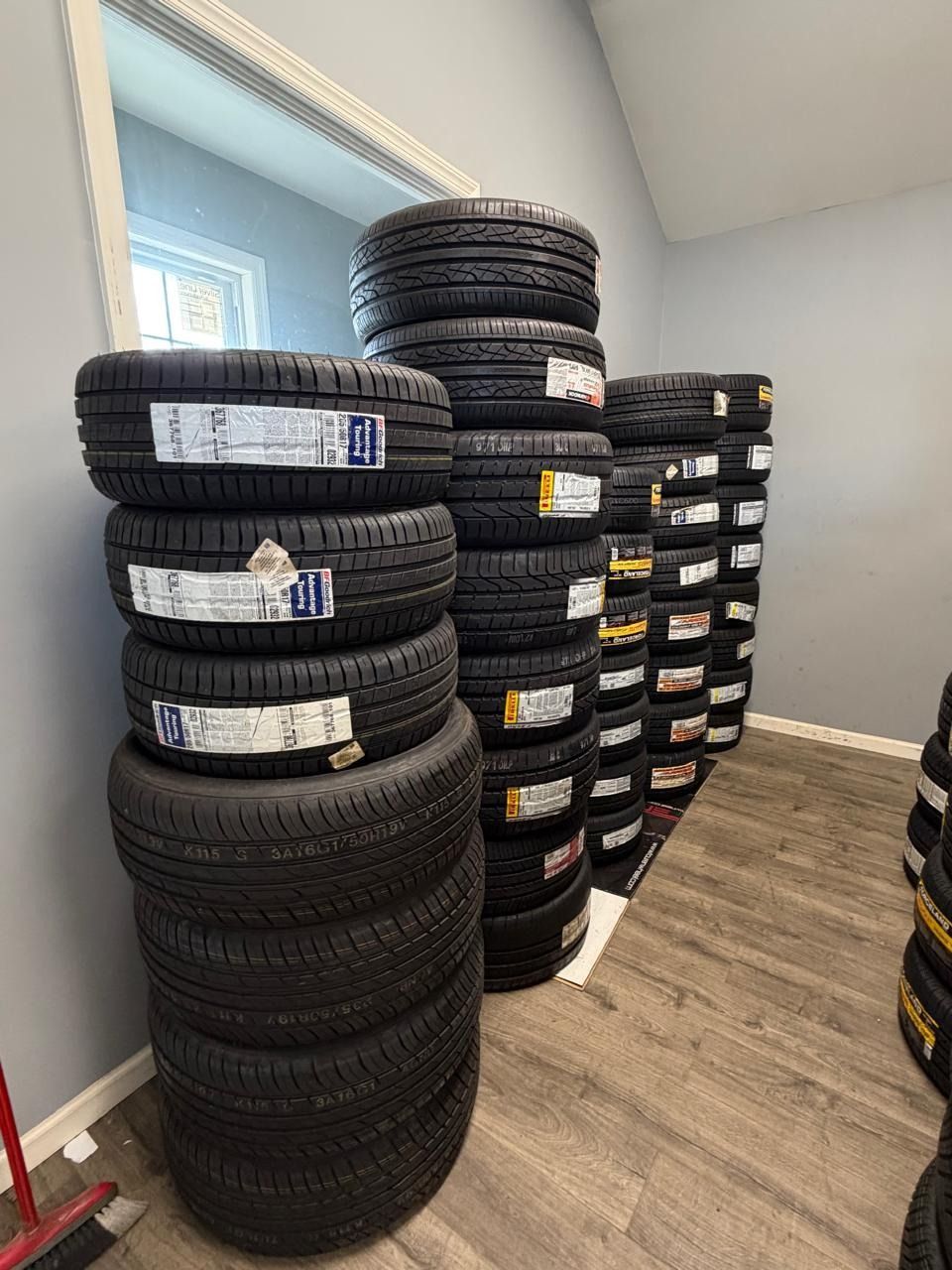 Stacks of black tires piled in a small room with wood flooring and a window.