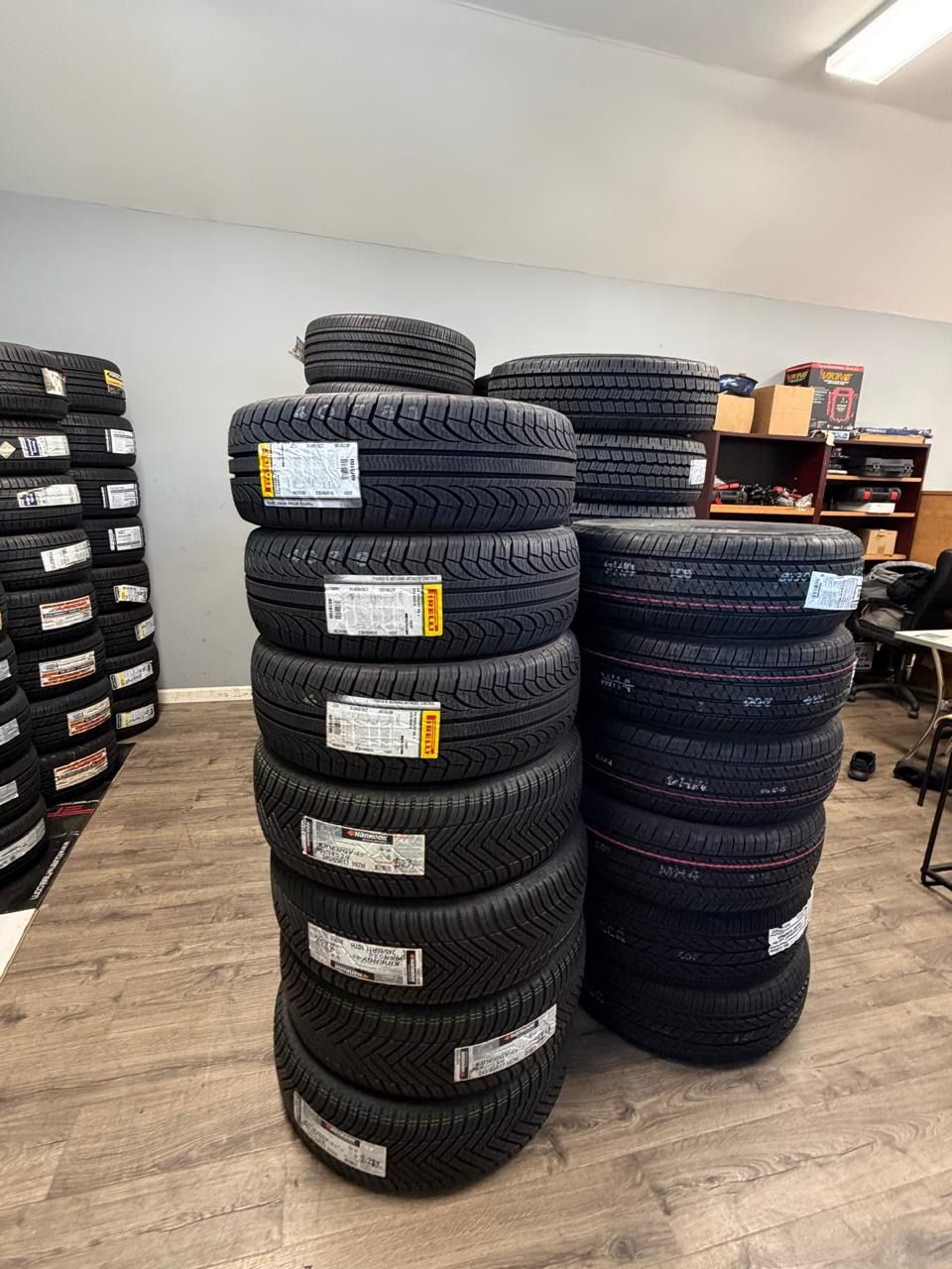 Stacks of black car tires in a workshop with shelves and a wooden floor.