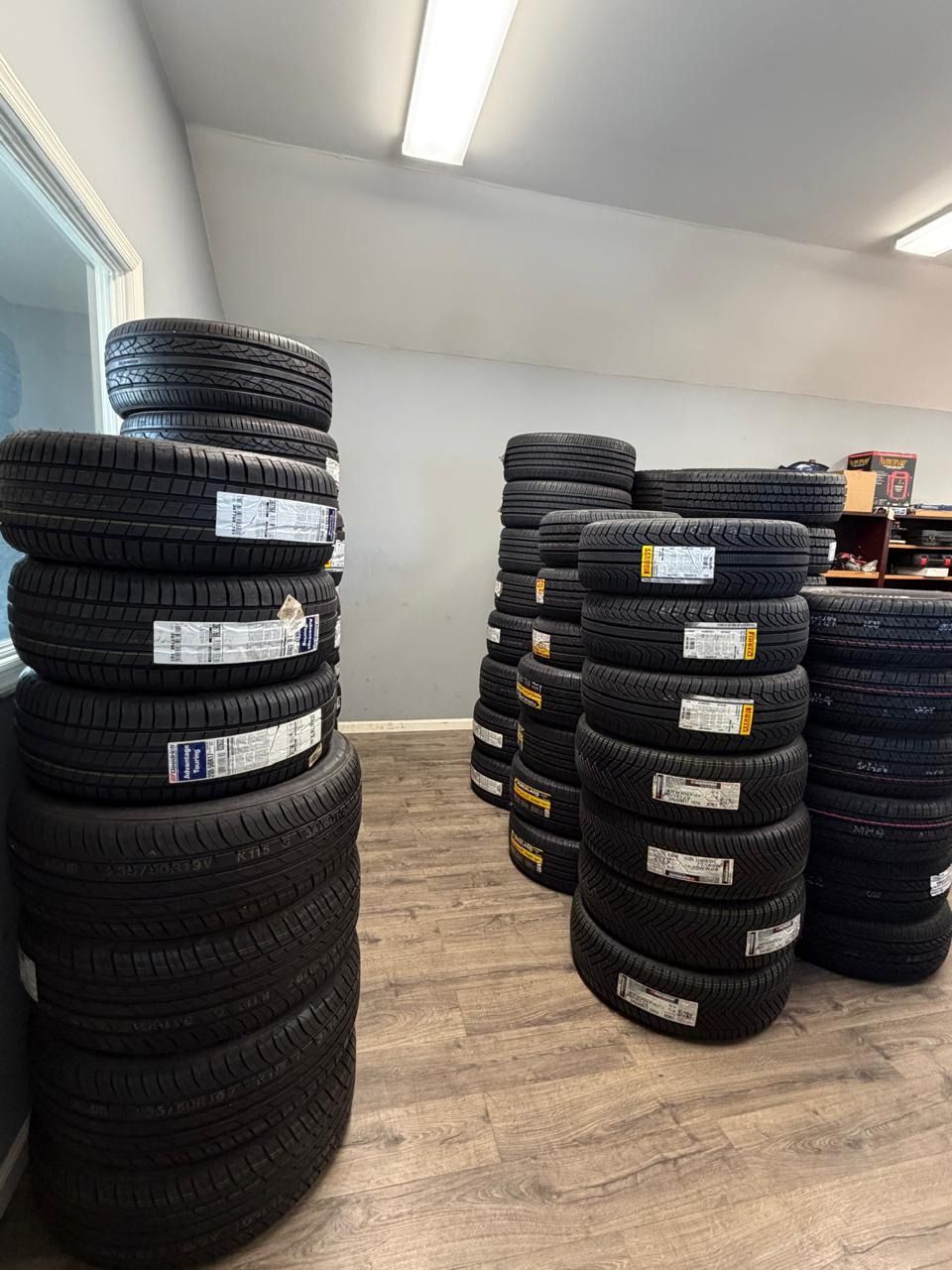 Stacks of car tires stored in a bright indoor room with light wood flooring.