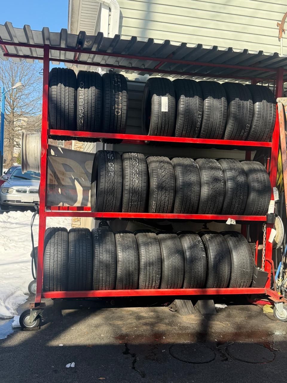 Red tire rack stacked with used tires outside a building in snowy daylight