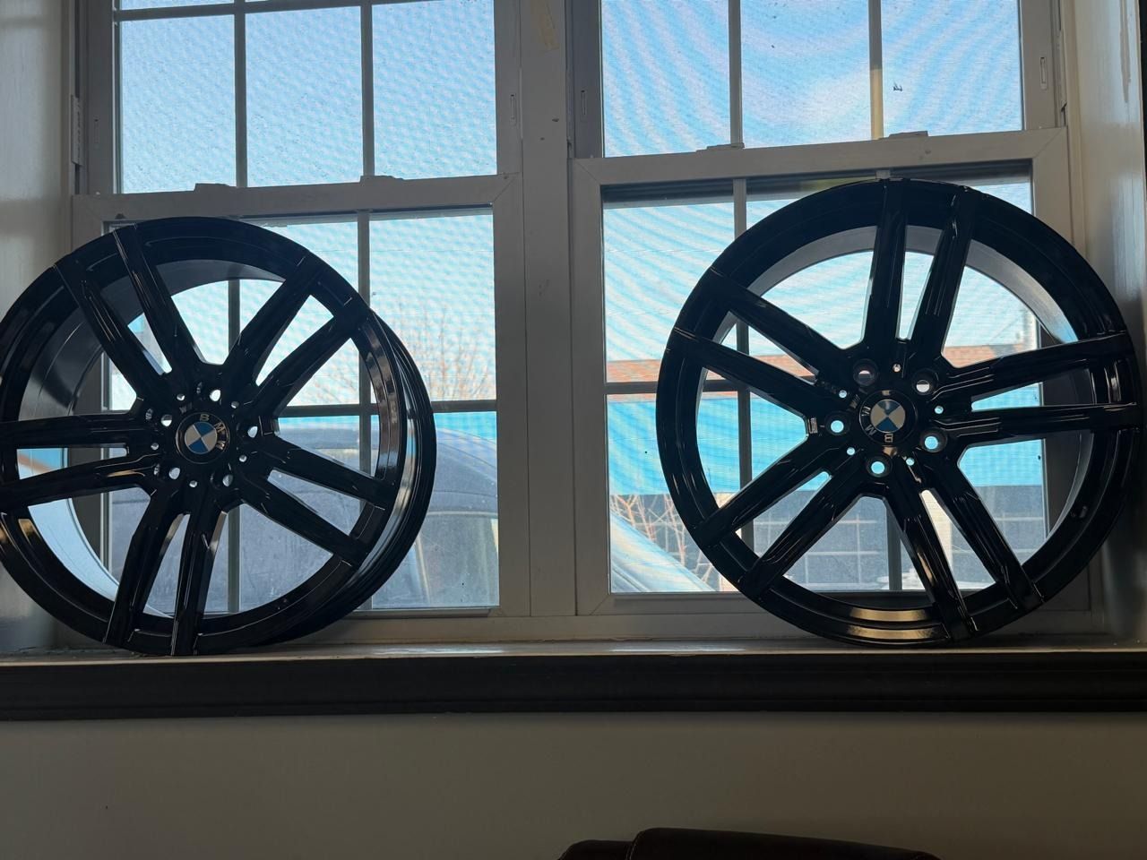 Two black alloy wheels displayed on a windowsill in front of a bright window