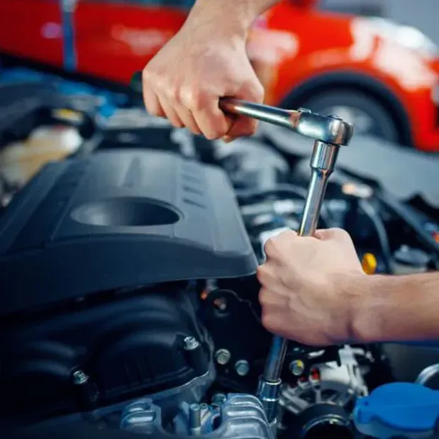 Mechanic tightening a bolt on a car engine with a ratchet in an auto shop