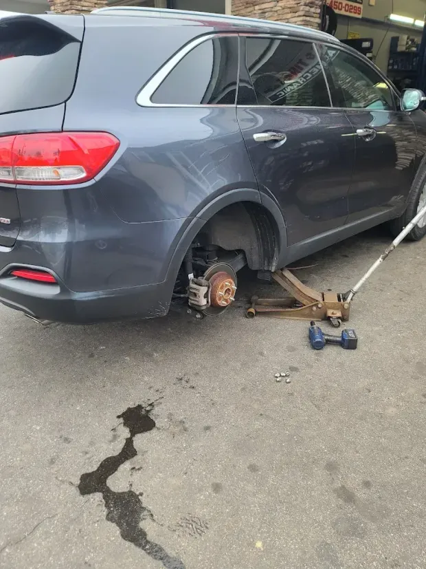 Gray SUV raised on a jack with the rear wheel removed, brake rotor exposed, and tools on the pavement.