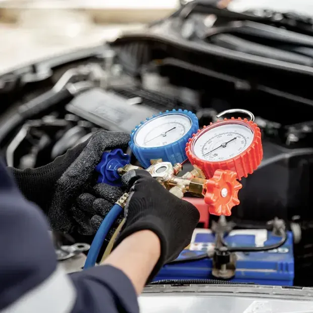 Mechanic connecting blue and red gauges to a car air-conditioning system under the hood