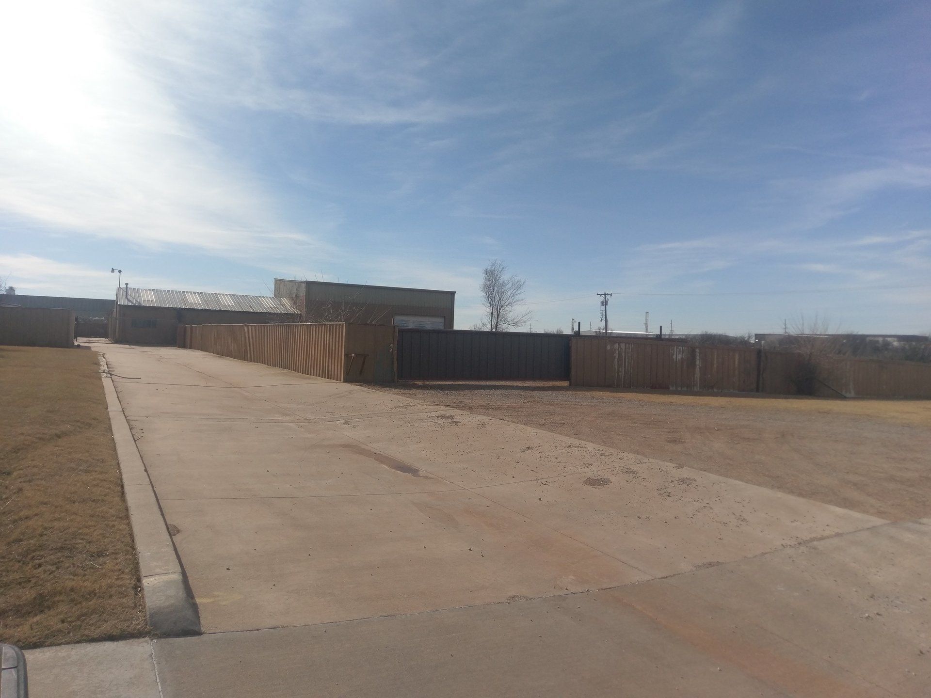 A long concrete driveway leading to a fenced industrial area 