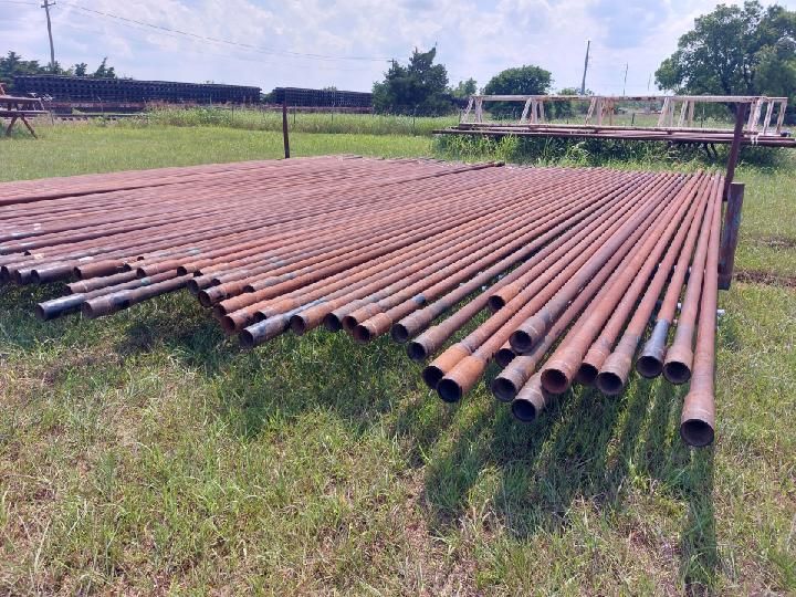 Rusty metal pipes stacked on a grassy field