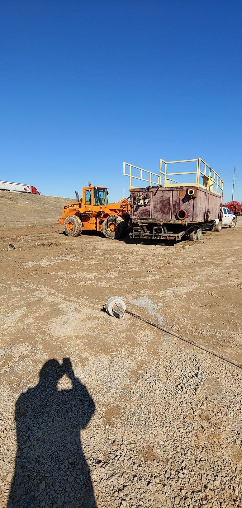 An orange bulldozer with a large, rusty tank on a gravel surface under a blue sky