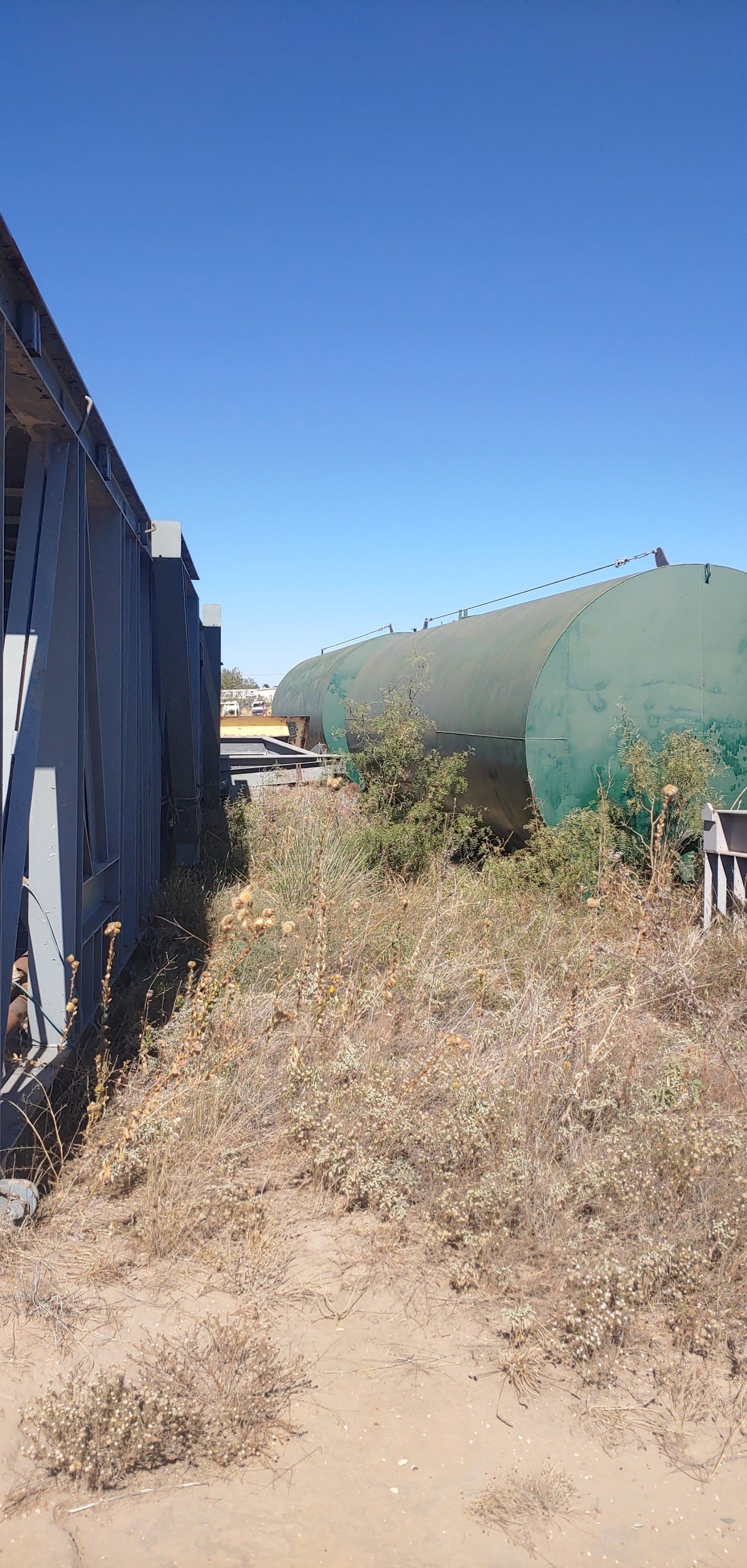 A gravel path between metal parts and green tanks under a clear blue sky