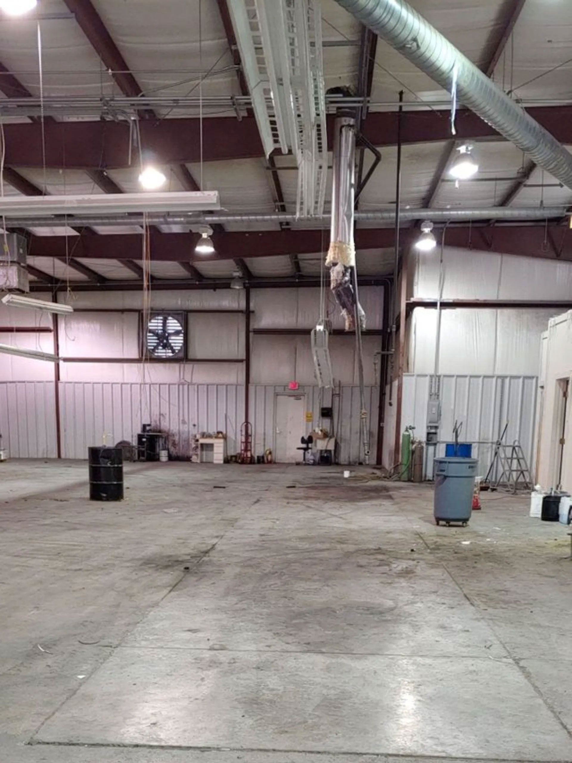 Interior of a warehouse with a concrete floor, metal beams, overhead lights, and equipment