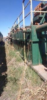 Green industrial machinery with white railing next to dry grass under a blue sky