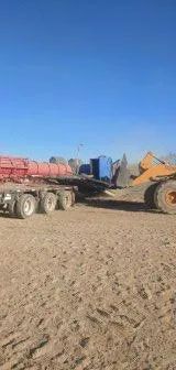 A truck with a red container and construction equipment on a brown field under a blue sky