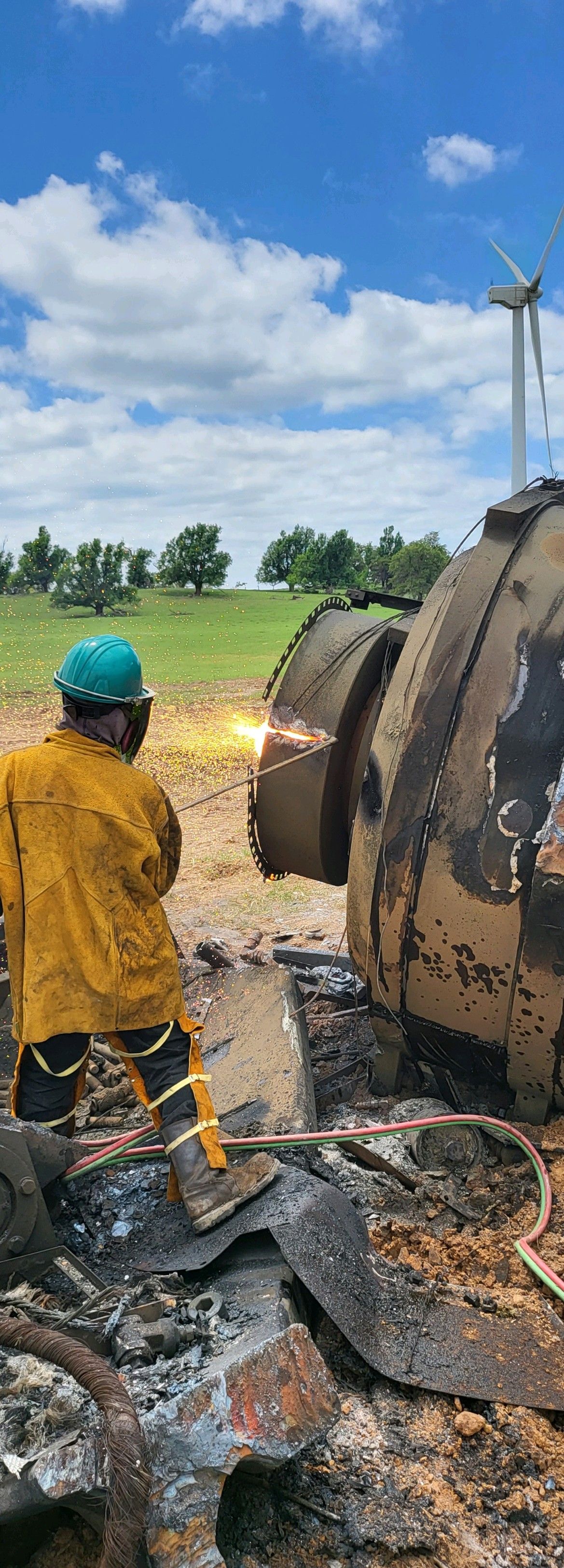 A person in safety gear using a torch to cut through a large metal object outdoors