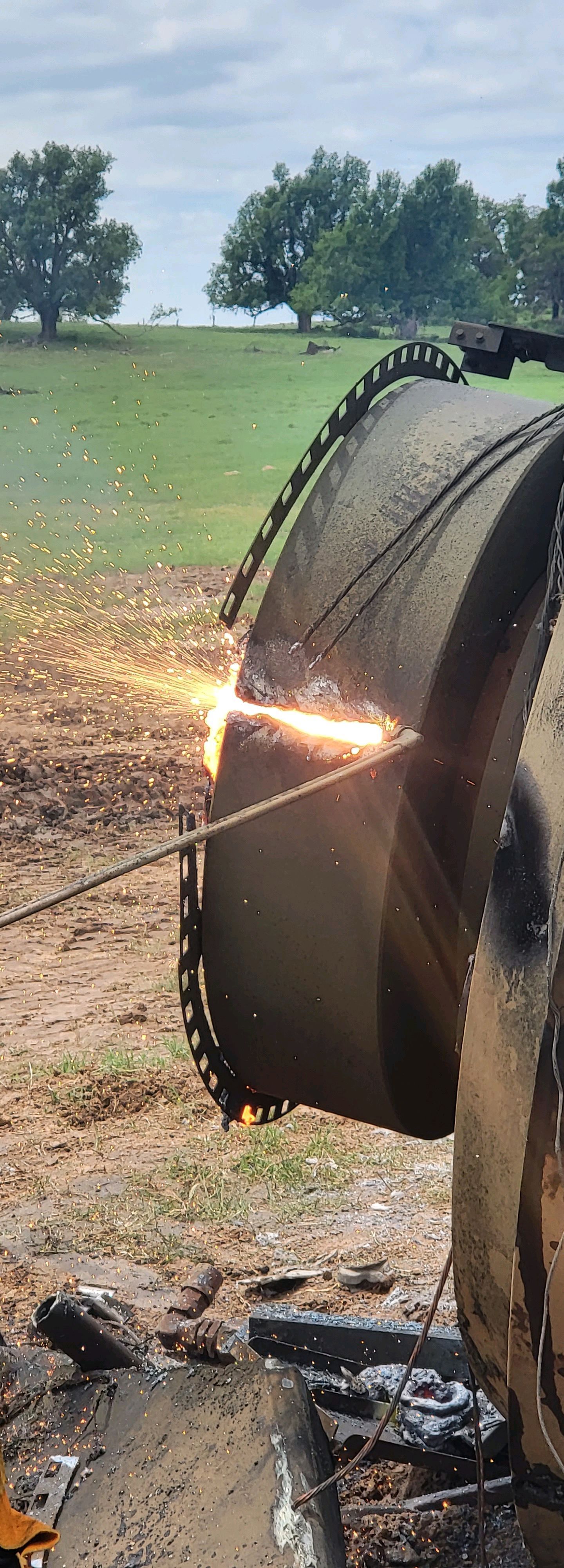 A person using a torch to cut through a large metal outdoors