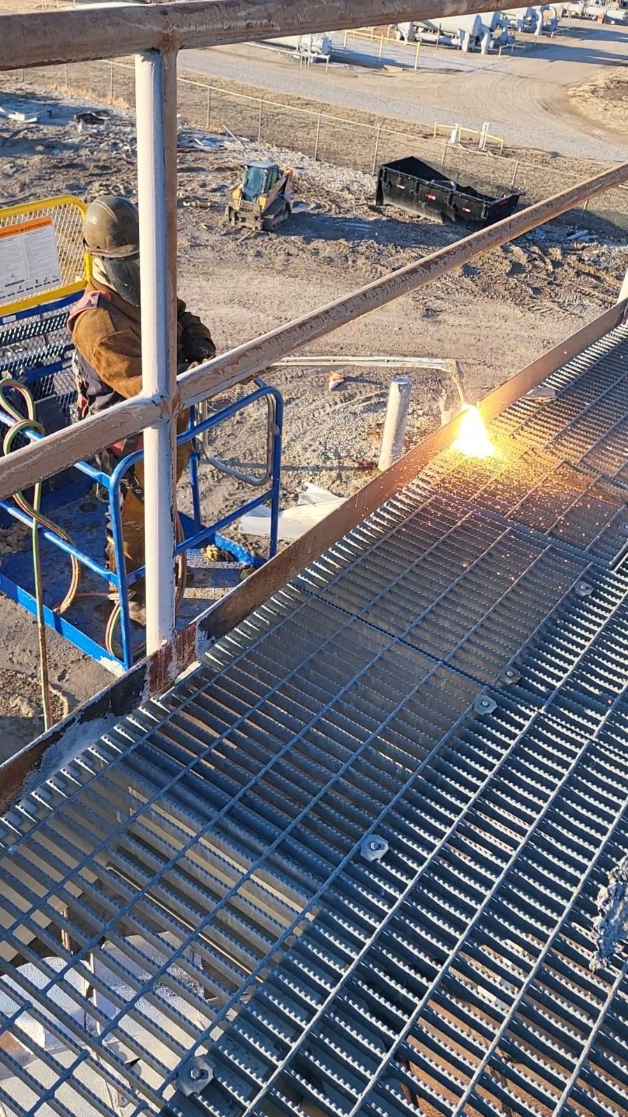 Person in protective gear welding metal grating on a platform