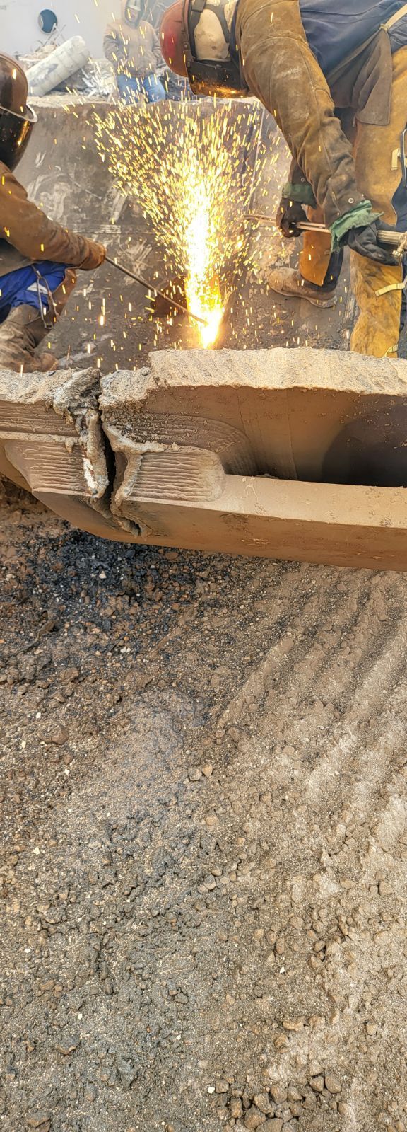 Two workers using a torch to cut through a wooden beam