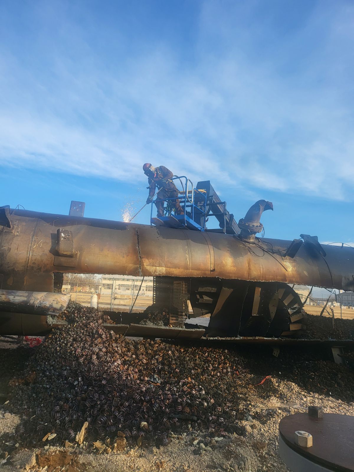 Workers use equipment on a damaged, dark-colored cylindrical structure