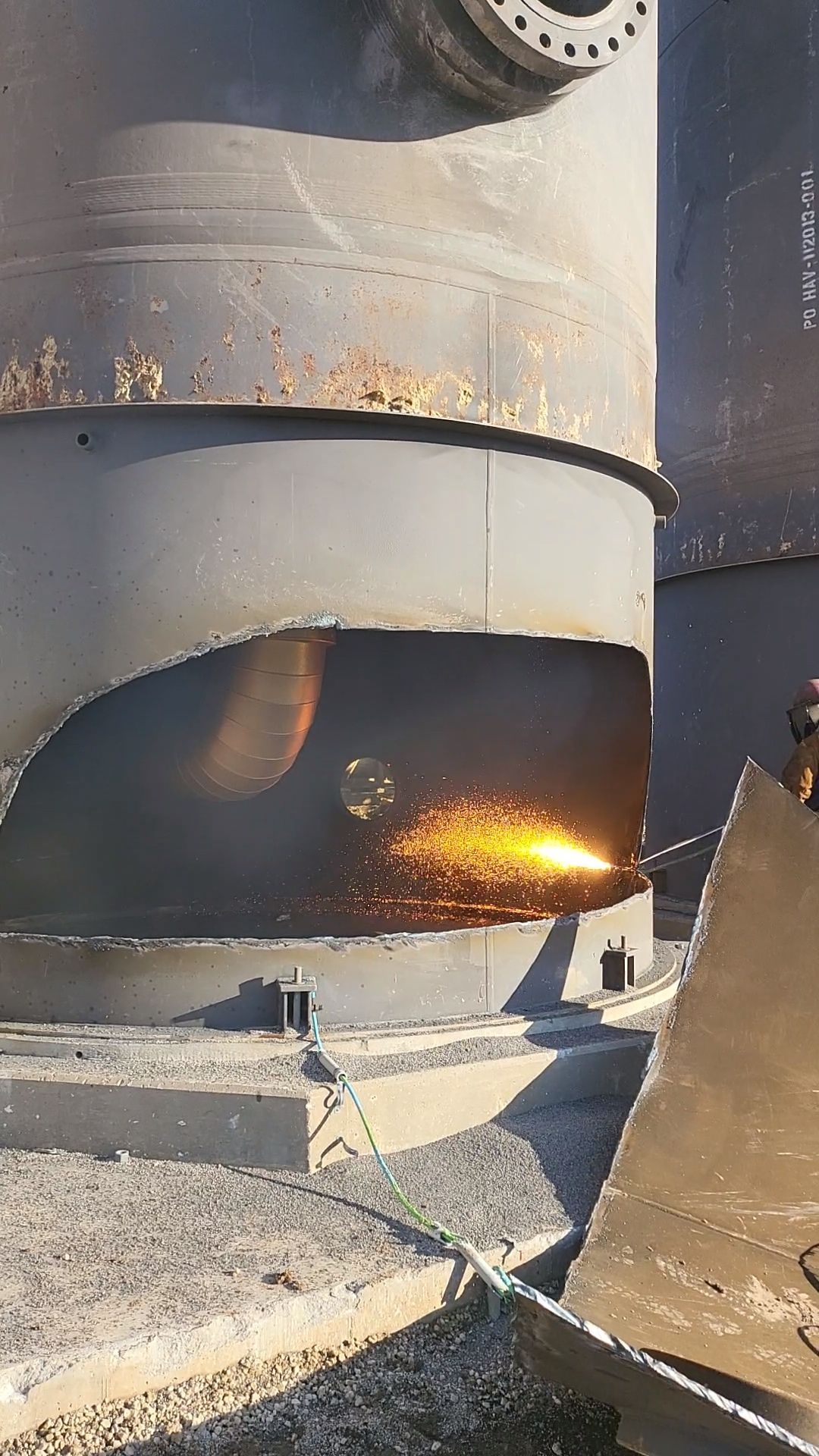 Worker using a cutting torch on a large metal industrial tank