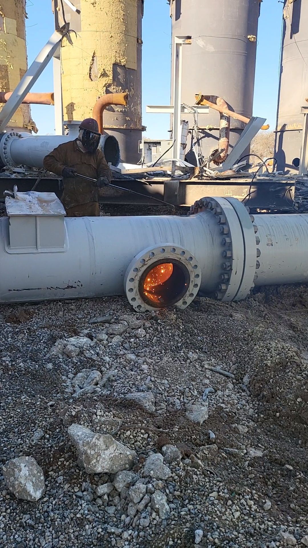 A person in protective gear stands near a damaged pipe 
