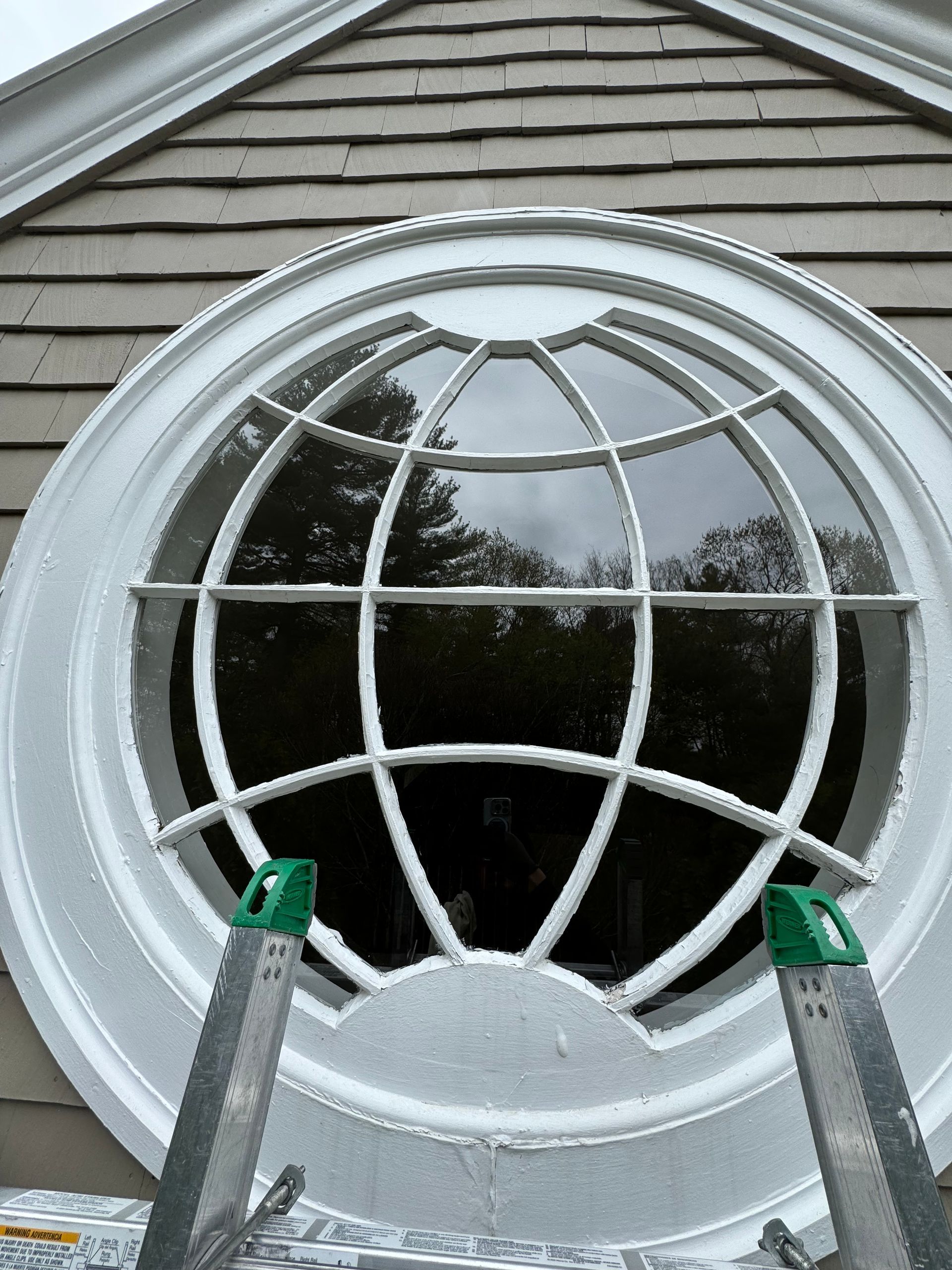 A round window on the side of a house with a ladder in front of it.