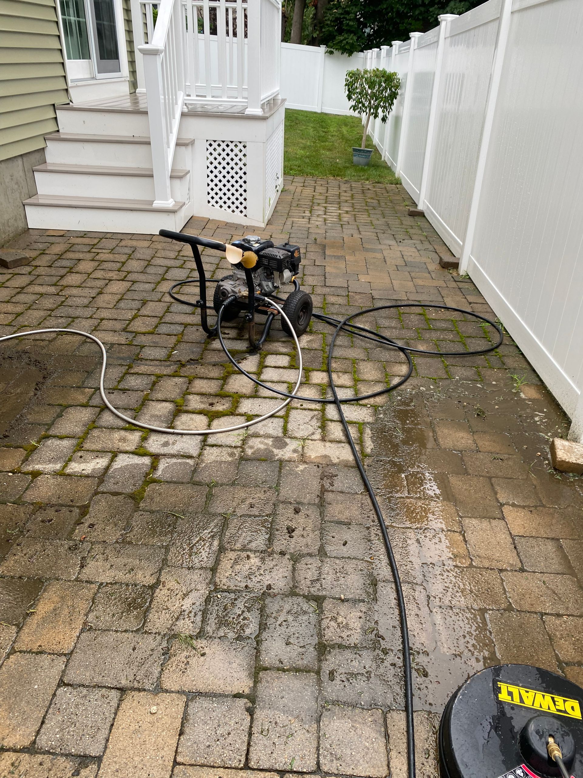 A pressure washer is being used to clean a brick patio.