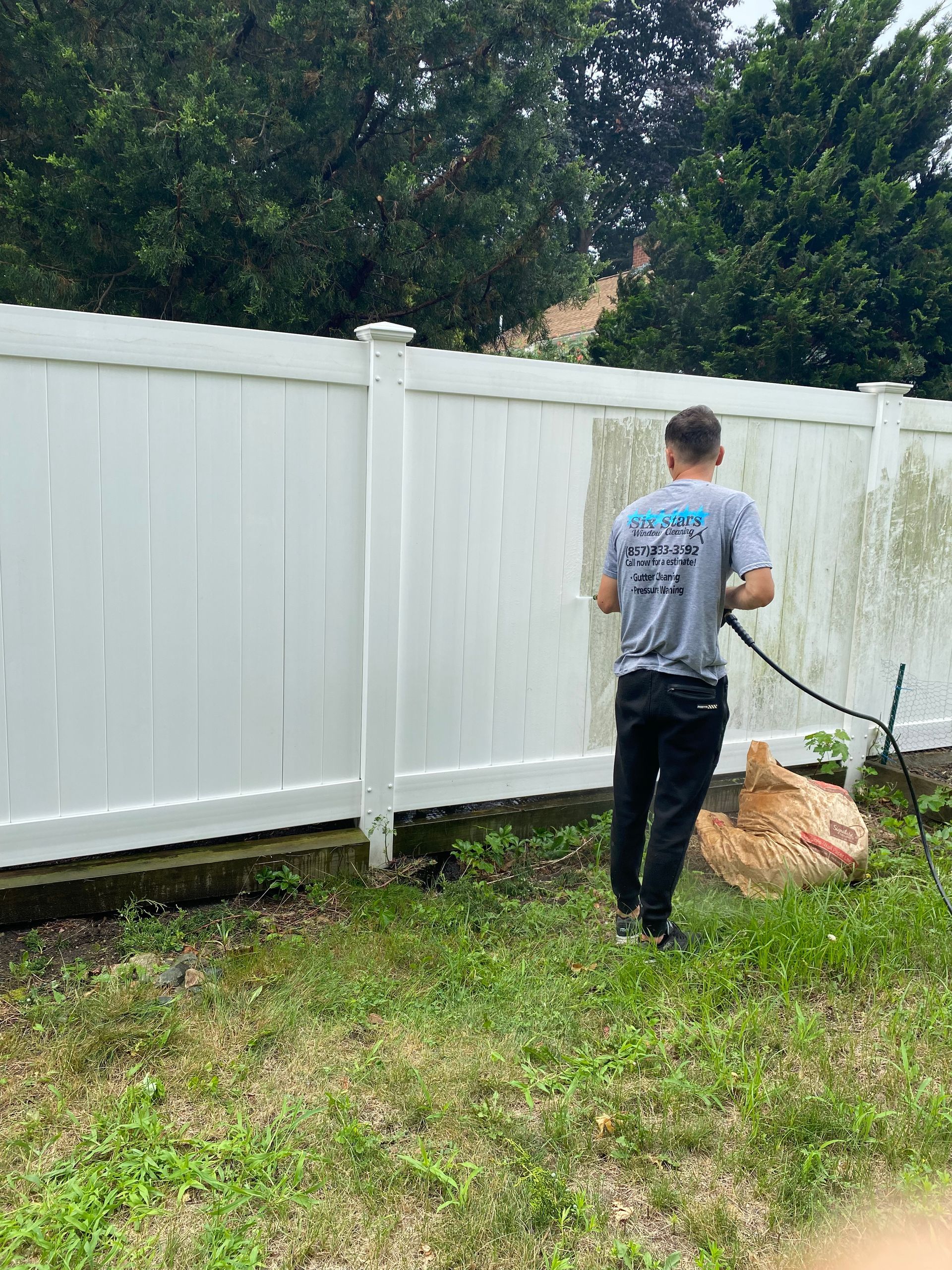 A man is cleaning a white fence with a hose.
