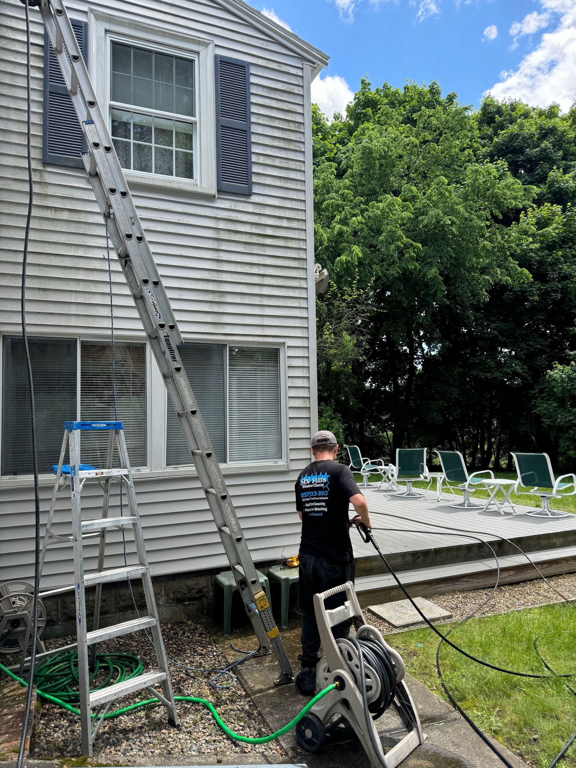 A man is cleaning the side of a house with a pressure washer.