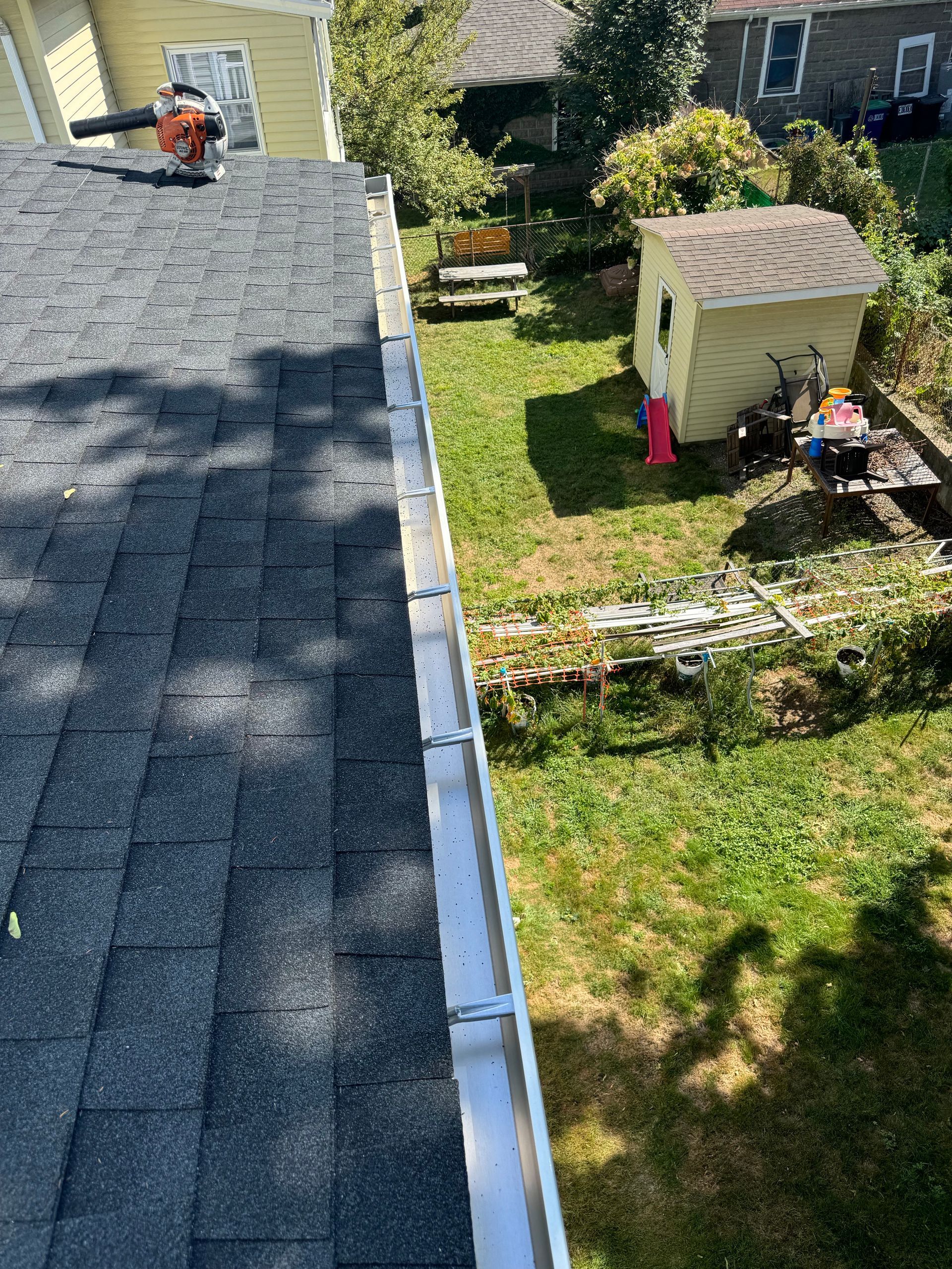 A roof with a gutter on it and a shed in the background.