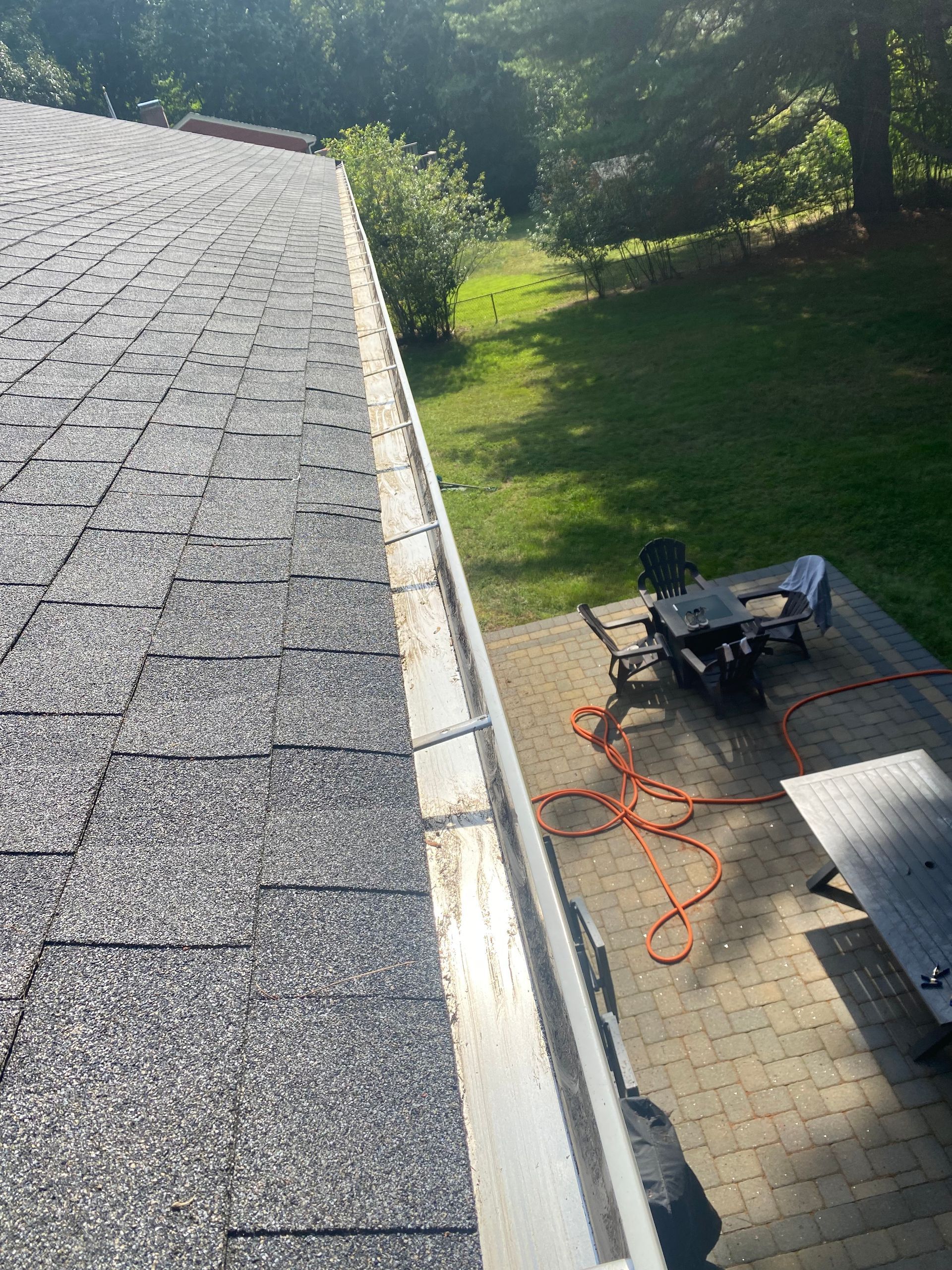 A roof with a gutter on it and a picnic table and chairs in the background.