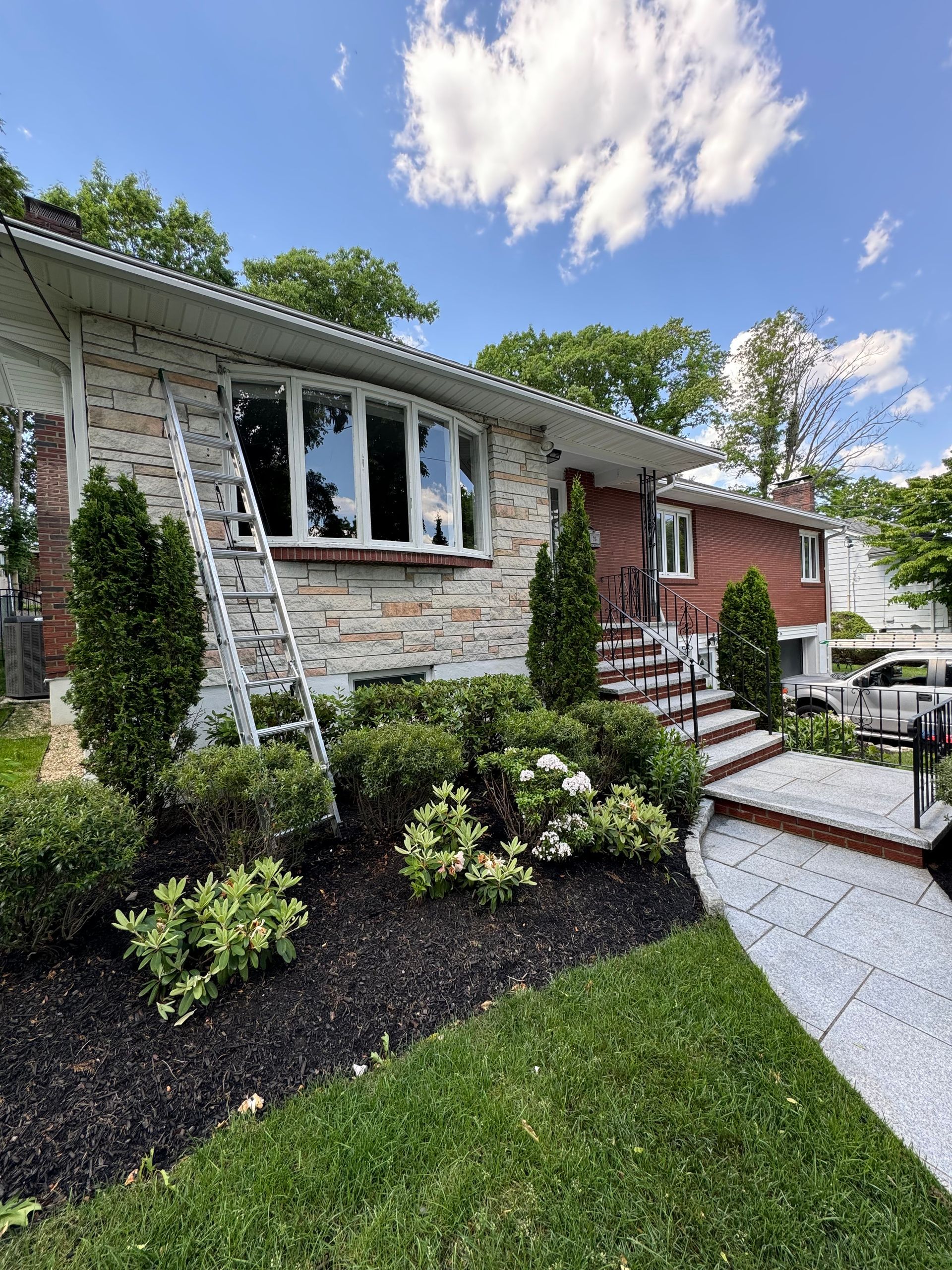 A brick house with a ladder in front of it is being painted.