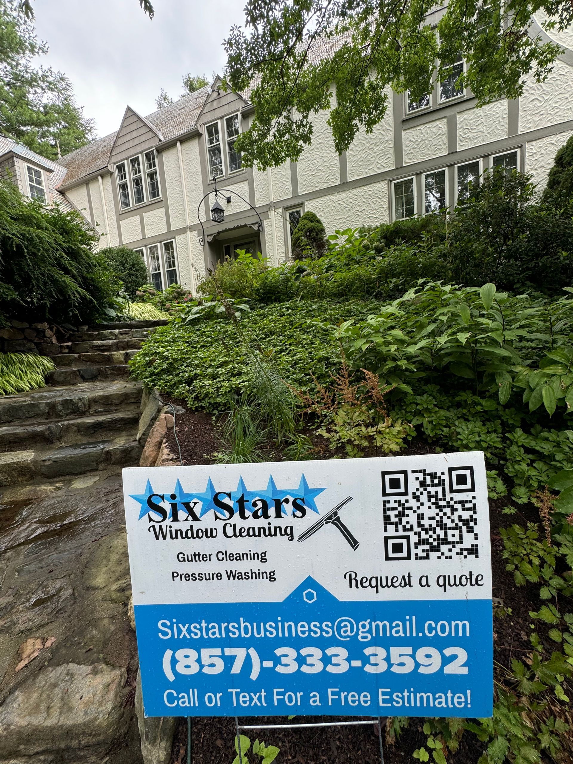A sign for six stars window cleaning is in front of a large house.