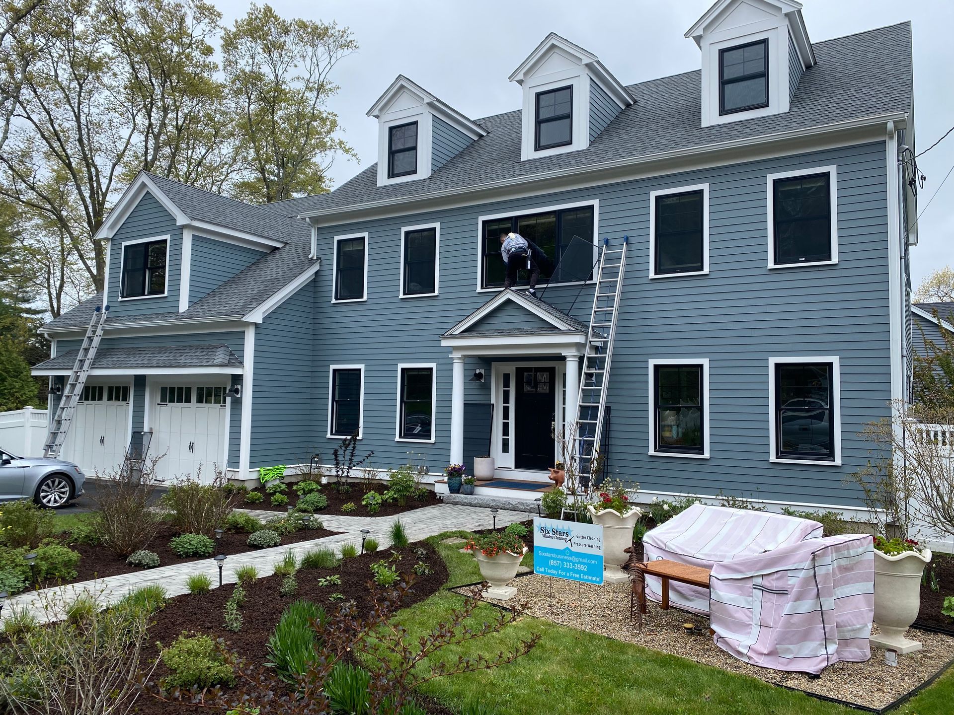A man is standing on a ladder in front of a large blue house.
