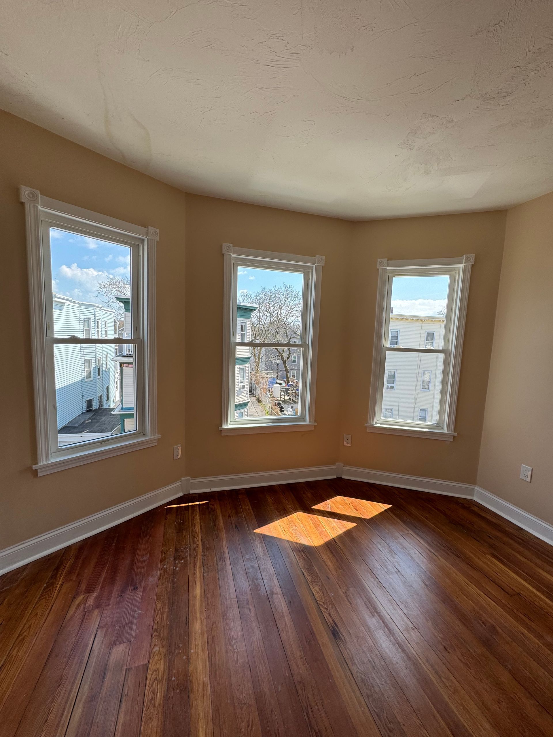 An empty room with hardwood floors and three windows.