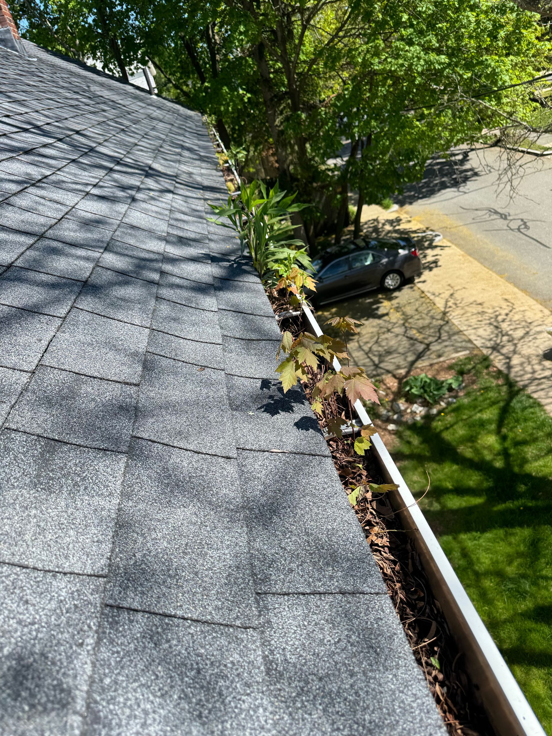 A close up of a gutter on a roof with a car parked in the background.