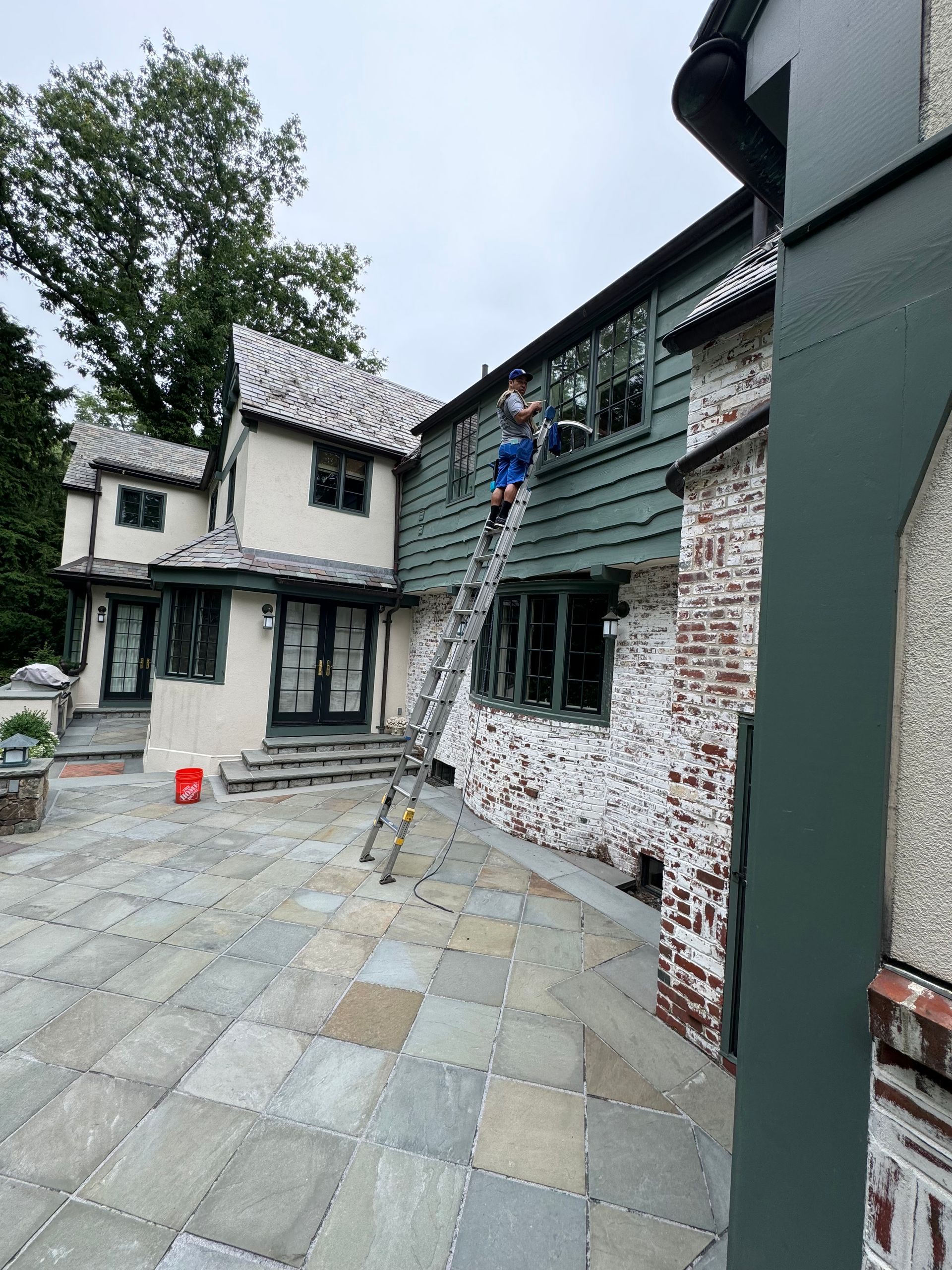 A man is standing on a ladder on the side of a house.