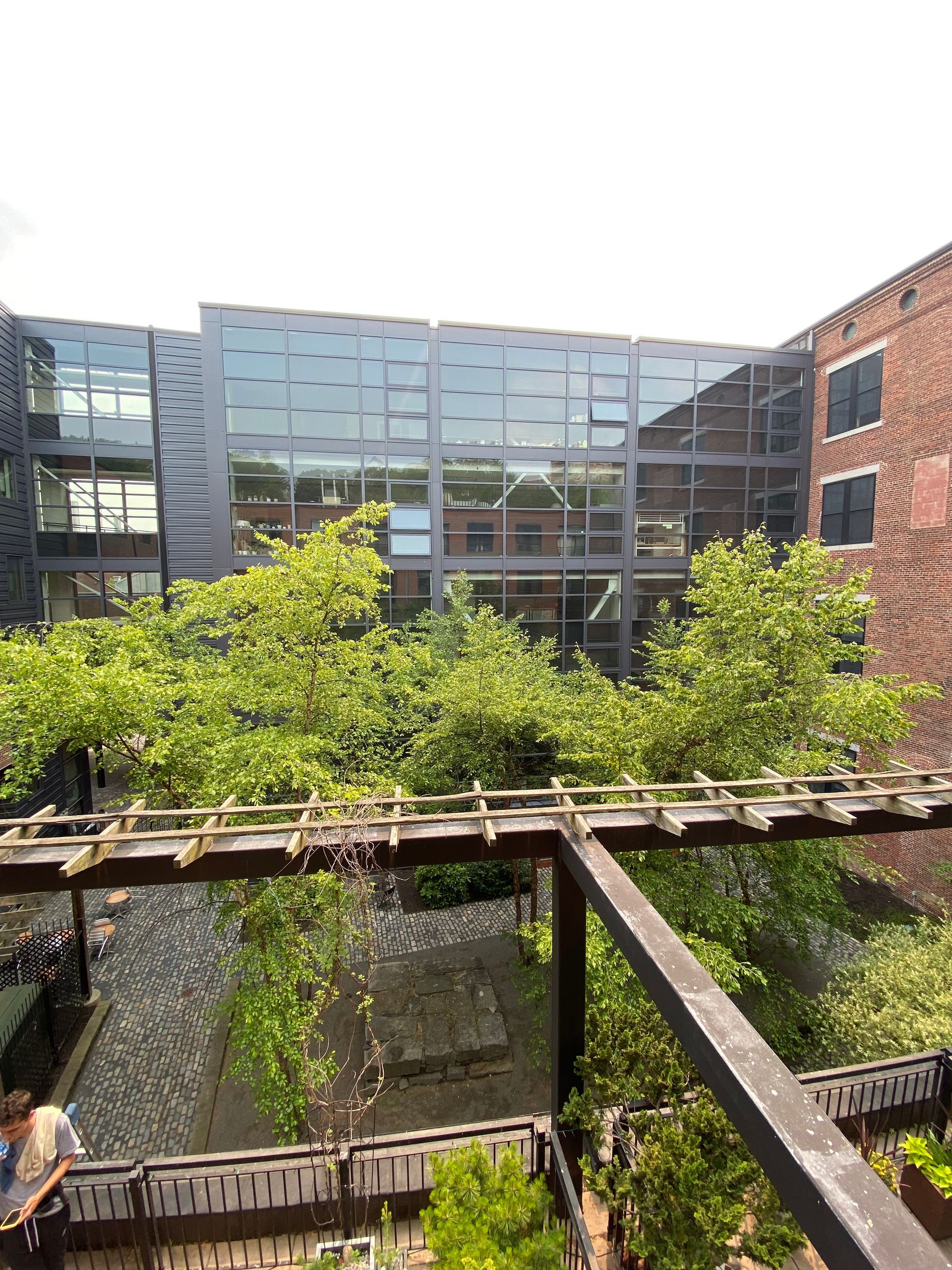 A large building with a lot of windows is surrounded by trees and a bridge.